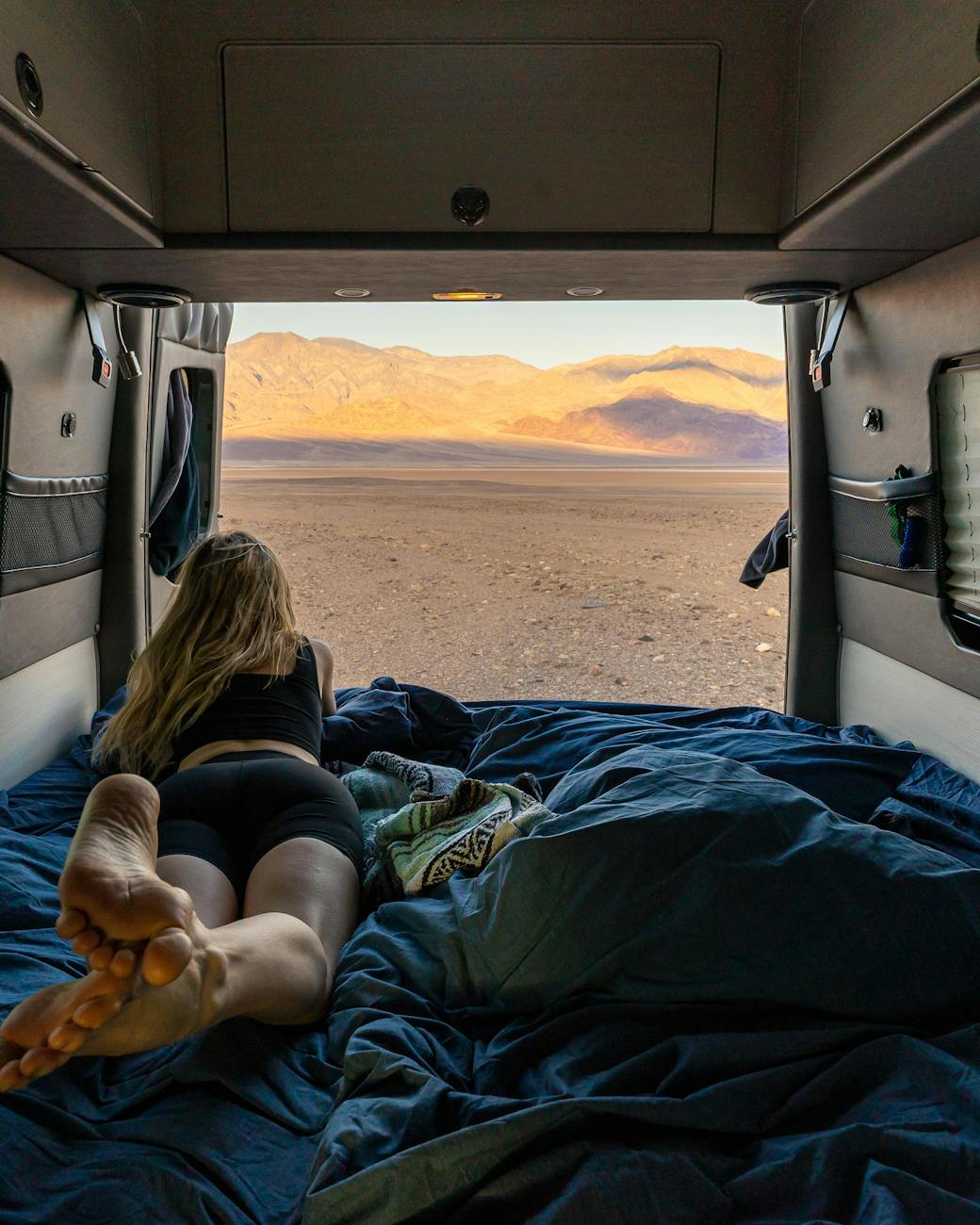 woman lying in a campervan with opened doors and looking at a desert landscape