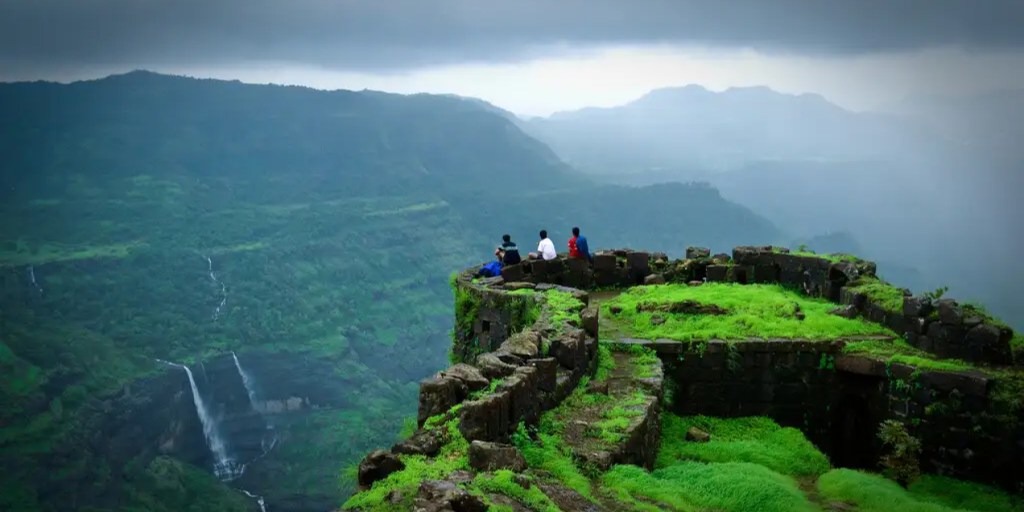 A breathtaking view of Rajmachi Fort in Lonavala during the monsoon, surrounded by lush greenery, misty hills, and cascading waterfalls.