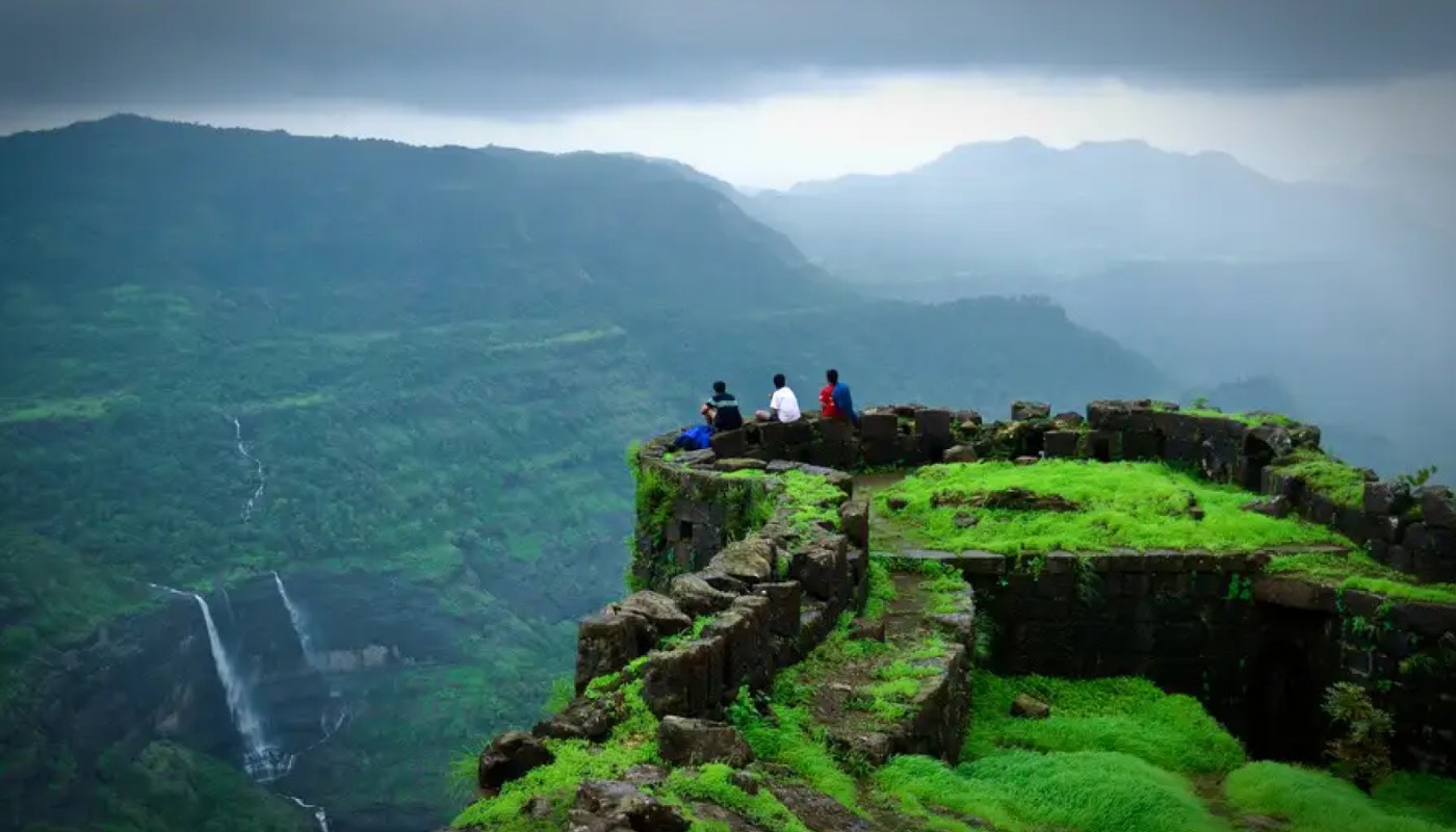 A breathtaking view of Rajmachi Fort in Lonavala during the monsoon, surrounded by lush greenery, misty hills, and cascading waterfalls.