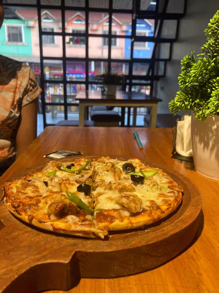 A beautifully presented pizza and refreshing drinks at an open-air café in Lonavala, surrounded by lush greenery and elegant decor