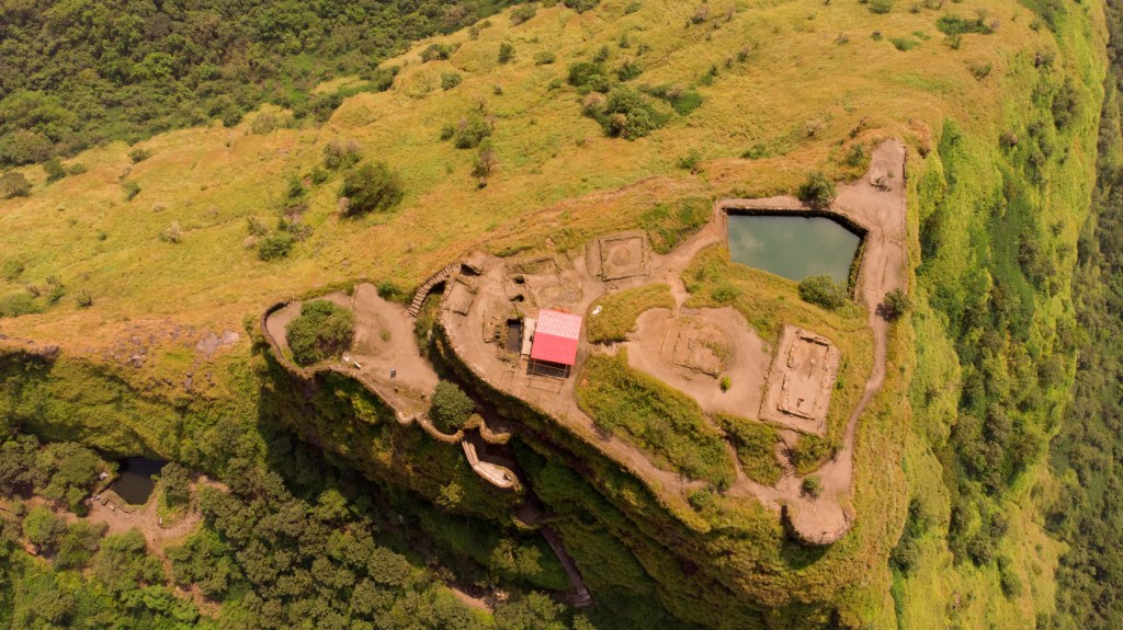 Scenic view of Tikona Fort during monsoon with clouds, greenery, and Pawna Lake in the backdrop
