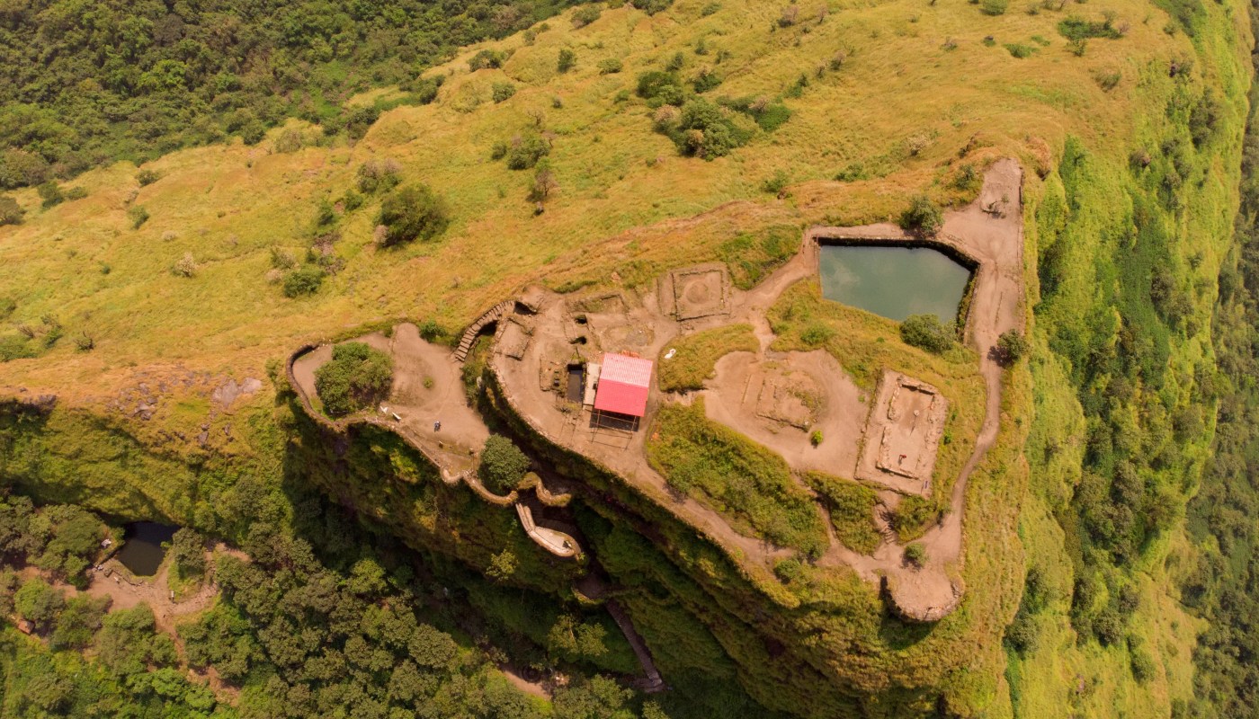 Scenic view of Tikona Fort during monsoon with clouds, greenery, and Pawna Lake in the backdrop