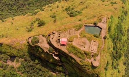 Scenic view of Tikona Fort during monsoon with clouds, greenery, and Pawna Lake in the backdrop