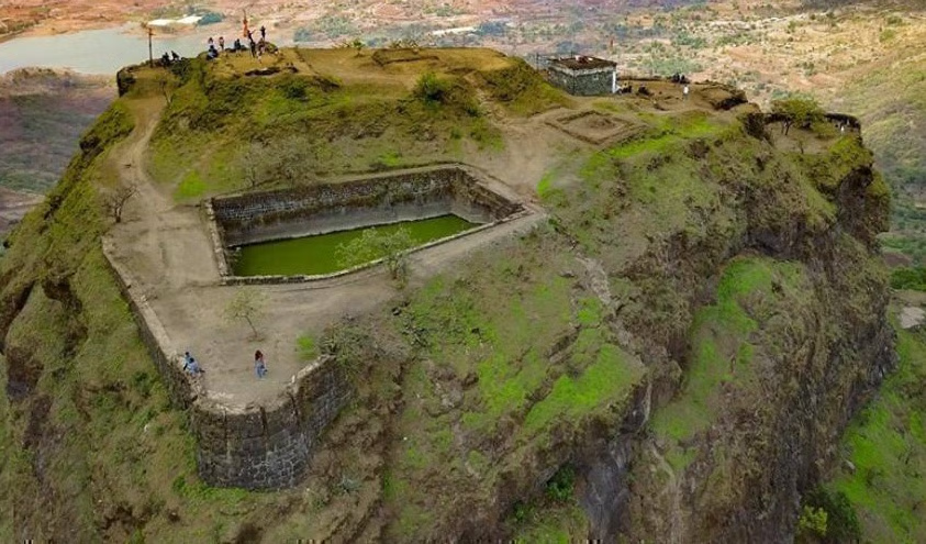 Scenic view of Tikona Fort during monsoon with clouds, greenery, and Pawna Lake in the backdrop