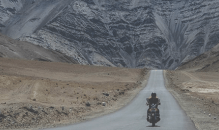 Bikers riding through mountain roads on Pune to Leh Ladakh route, passing high-altitude landscapes.