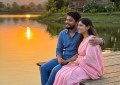 Couple sitting by a calm lake at sunset, wooden cottage in background, warm golden light, peaceful Pune countryside