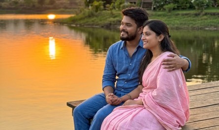 Couple sitting by a calm lake at sunset, wooden cottage in background, warm golden light, peaceful Pune countryside
