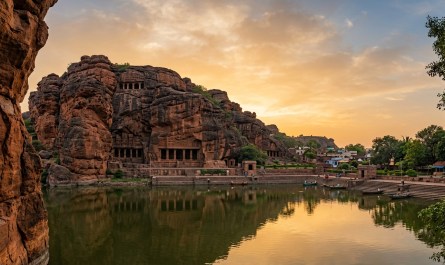 Early morning view of ancient Badami cave temples carved into red sandstone cliffs overlooking Agastya Lake, golden hour