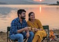 Couple sitting on camping chairs by Pawna Lake at golden hour, soft sunset light, wide angle, warm tones, candid moment