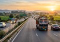 Two-lane Indian highway at dawn, trucks and cars, golden hour light, wide-angle road trip perspective