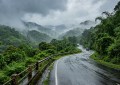 Misty Western Ghats road through green hills during light monsoon rain, wet asphalt, soft natural lighting, wide-angle v