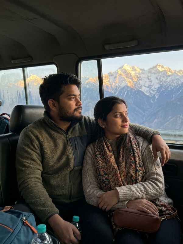 Young Indian couple in shared taxi looking out at snow-capped Kashmir peaks, golden hour light, candid travel moment, wa