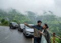 Wide-angle shot of cars parked along a scenic monsoon viewpoint road near Pune, misty hills in background, natural light