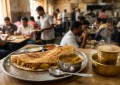 Golden masala dosa on steel plate, steaming filter coffee in traditional tumbler, morning sunlight, busy local restauran