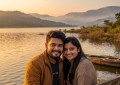Couple sitting by Mulshi Lake during golden hour with mist-covered hills in background, warm natural light, wide landsca