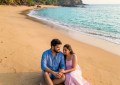 Aerial view of Cola Beach lagoon at sunrise, turquoise water meeting golden sand, couple sitting by the shore, soft morn