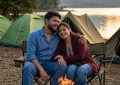 Couple sitting by bonfire at Pawna Lake camping with tents and hills in background, golden hour lighting, candid moment