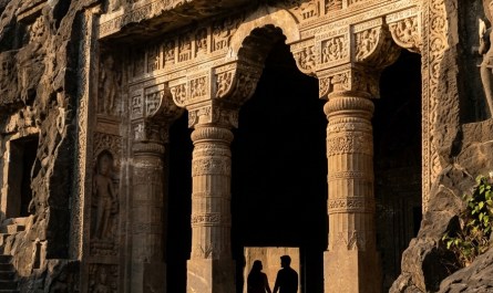 Ancient rock-cut Buddhist cave entrance carved into basalt hillside, afternoon sunlight illuminating octagonal stone pil