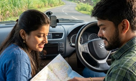 Young couple checking paper map inside car parked on rural Maharashtra road, morning light, dashboard visible, green hil