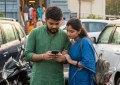 Indian couple checking phone at temple parking lot, early morning light, candid travel moment, realistic documentary sty