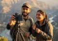 Indian couple filming travel vlog with smartphone on tripod at scenic viewpoint, golden hour lighting, natural candid in