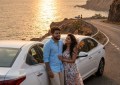 Indian couple standing beside car on coastal highway overlooking Arabian Sea, golden hour light, wide-angle shot showing
