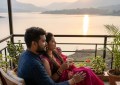 Couple sitting on a private cottage balcony overlooking Mulshi Lake at sunrise, soft golden light, intimate and serene c